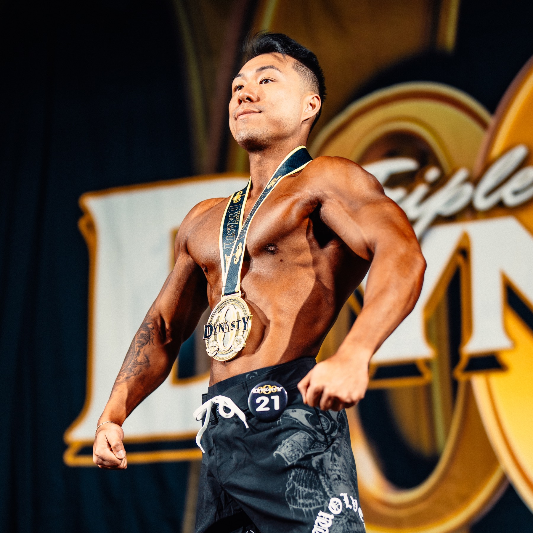 Coach Zack on stage at a physique competition, wearing a medal